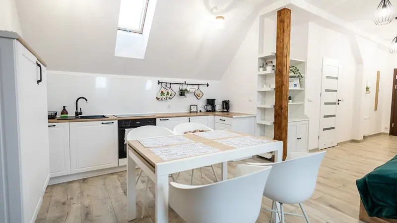 Kuchnia z białymi szafkami, drewnianym blatem i stołem.